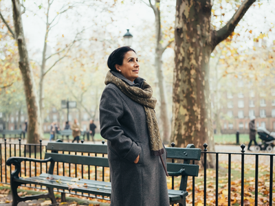 Woman in her fifties walking through an autumnal London park.