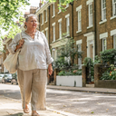 Woman in her fifties walking through a leafy West London street on a bright morning.