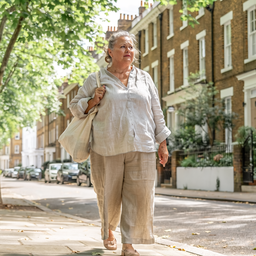 Woman in her fifties walking through a leafy West London street on a bright morning.