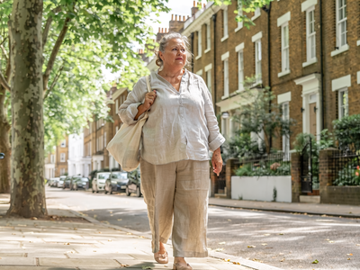 Woman in her fifties walking through a leafy West London street on a bright morning.