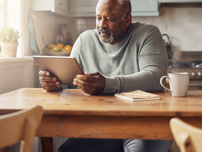 A Black British man in his fifties reading a wellness chart on a tablet at a sunlit kitchen table.