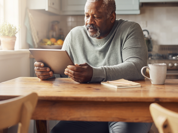 A Black British man in his fifties reading a wellness chart on a tablet at a sunlit kitchen table.