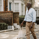 Man in his late forties walking along a leafy residential London street on a sunny weekday morning.