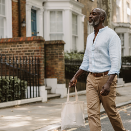 Man in his late forties walking along a leafy residential London street on a sunny weekday morning.