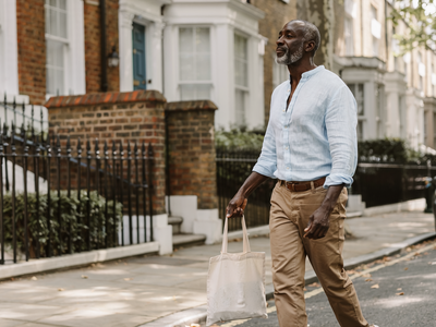 Man in his late forties walking along a leafy residential London street on a sunny weekday morning.