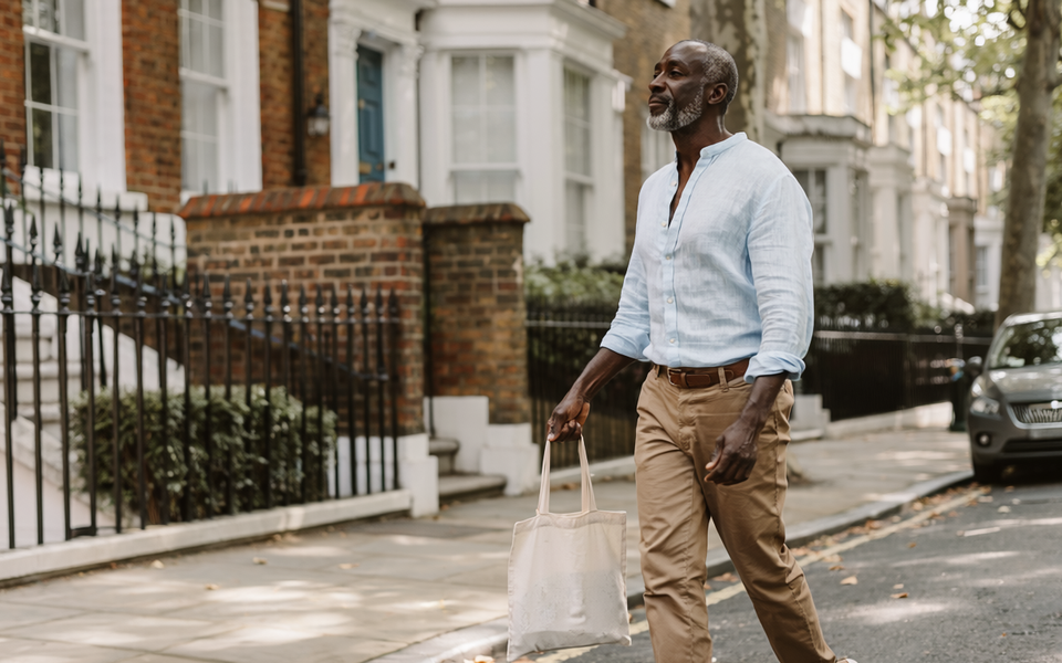 Man in his late forties walking along a leafy residential London street on a sunny weekday morning.