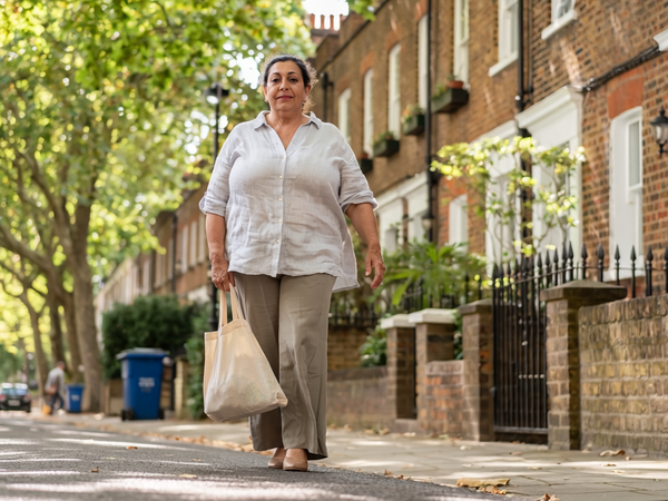 Woman in her fifties walking through a leafy West London street on a bright morning.