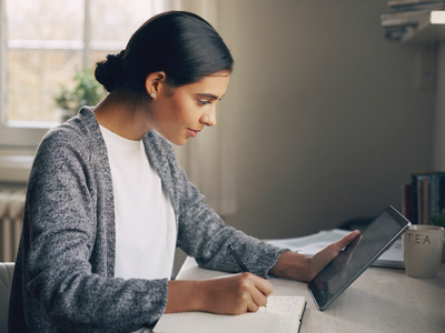 South Asian adult at home, focused on a notebook in natural daylight.