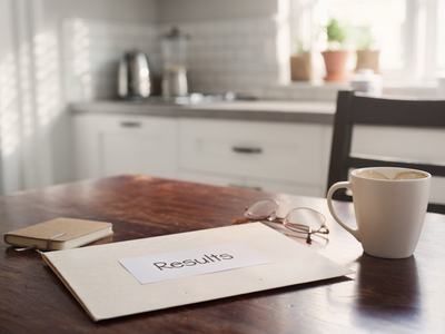 A folder marked Results on a sunlit kitchen table with a coffee mug and reading glasses.