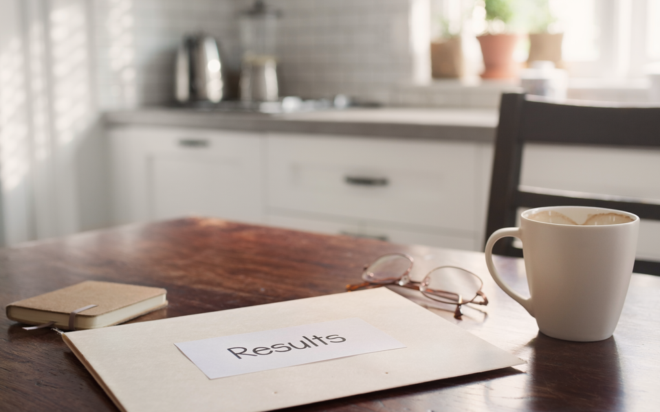 A folder marked Results on a sunlit kitchen table with a coffee mug and reading glasses.
