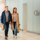 Two Londoners walking past a clinic frontage inside Westfield London on a bright weekday morning.
