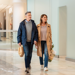 Two Londoners walking past a clinic frontage inside Westfield London on a bright weekday morning.