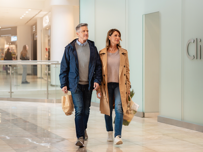 Two Londoners walking past a clinic frontage inside Westfield London on a bright weekday morning.
