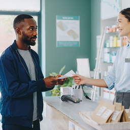 A person collecting a prescription at a UK community pharmacy counter, everyday high-street setting