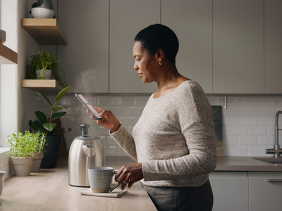 Woman in her fifties at home in a calm kitchen, making tea in the morning light.