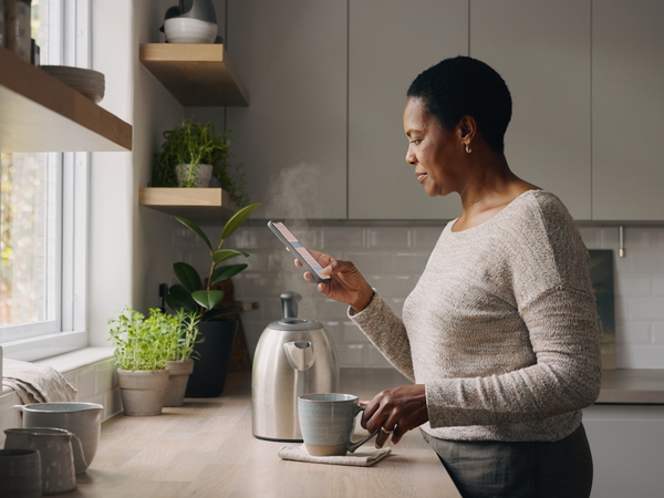 Woman in her fifties at home in a calm kitchen, making tea in the morning light.