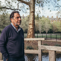 Man in his late forties walking across a wooden footbridge in a London park.