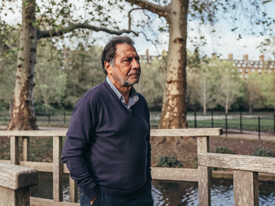 Man in his late forties walking across a wooden footbridge in a London park.