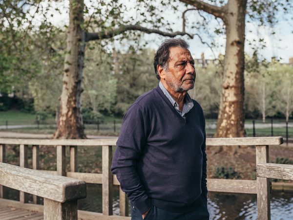 Man in his late forties walking across a wooden footbridge in a London park.