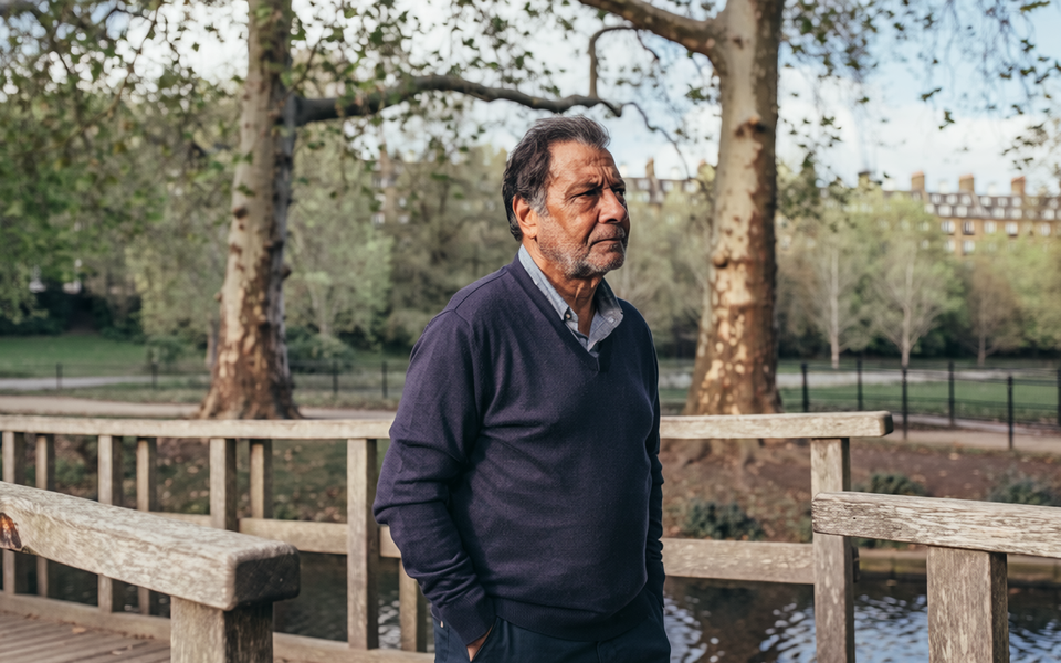 Man in his late forties walking across a wooden footbridge in a London park.