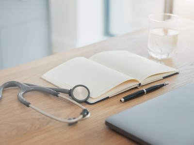 A close-up of a tidy doctor's desk with stethoscope, notebook, and fountain pen in soft natural daylight.