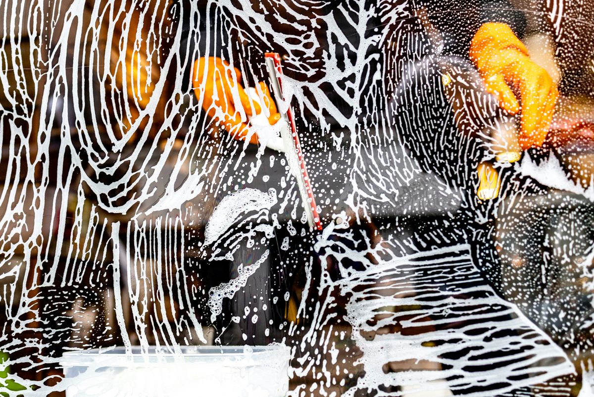 Window covered with soap suds and streaks, with blurred reflections of orange and black in the background, creating an abstract pattern.