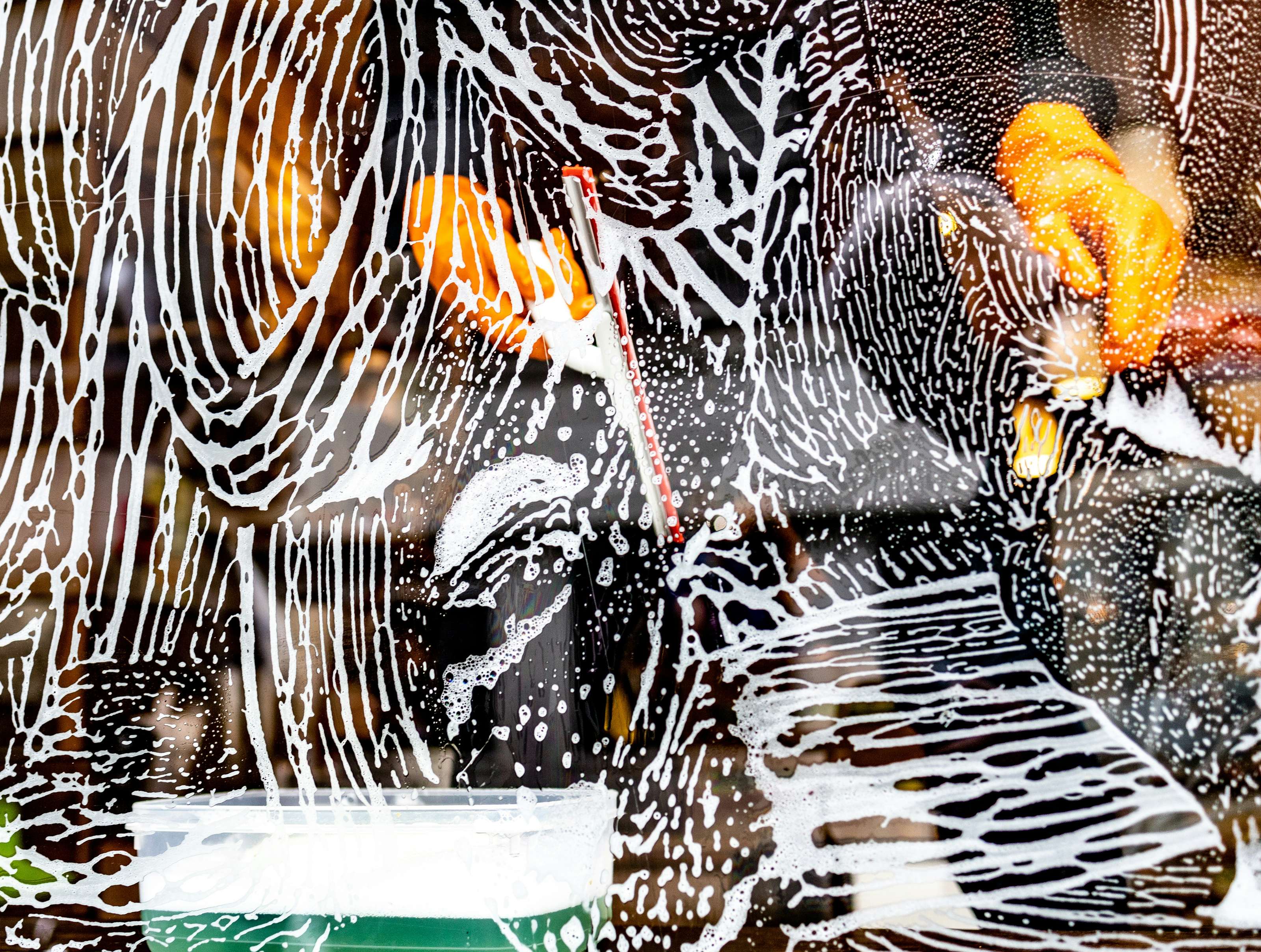 Window covered with soap suds and streaks, with blurred reflections of orange and black in the background, creating an abstract pattern.