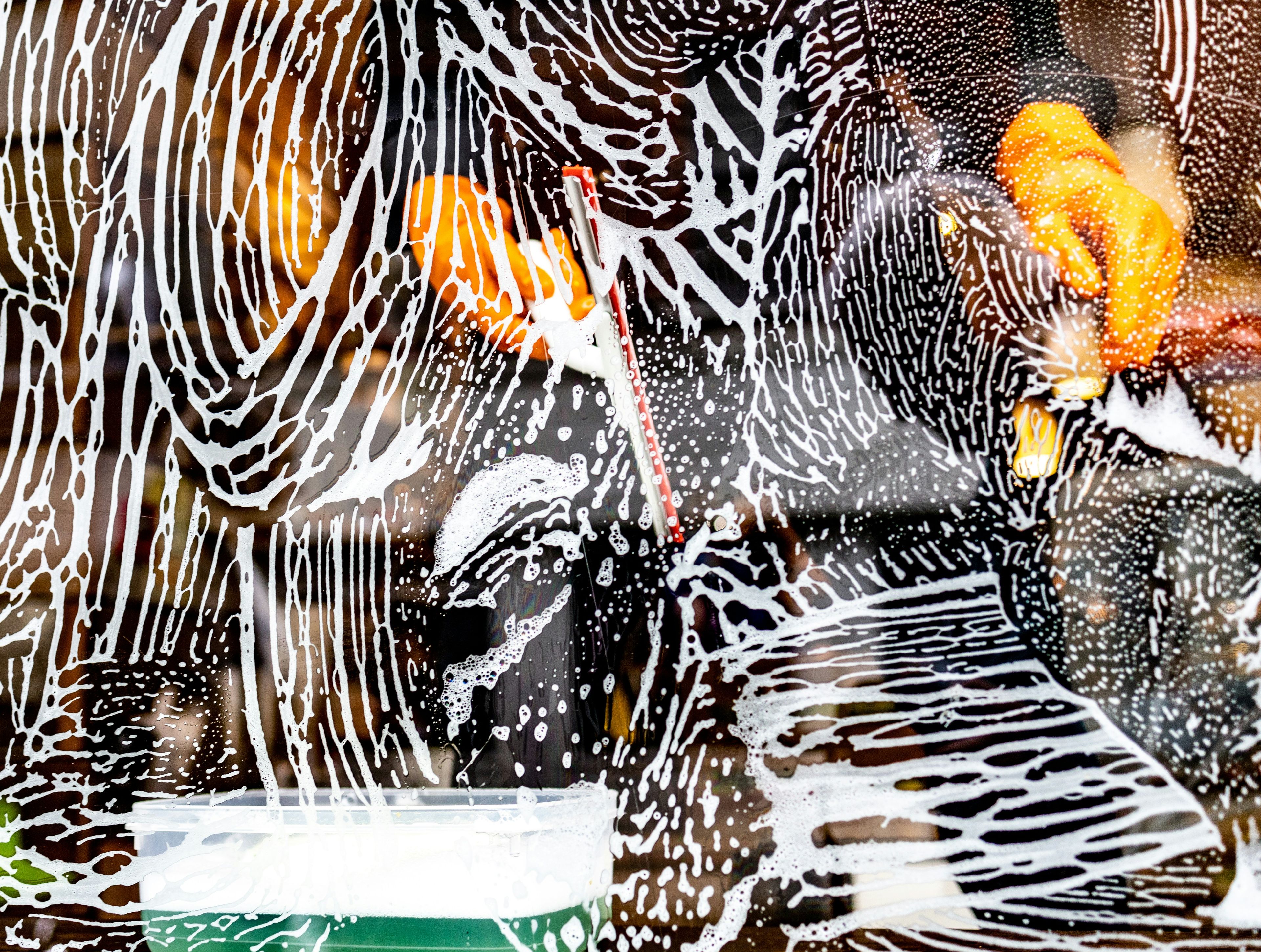 Window covered with soap suds and streaks, with blurred reflections of orange and black in the background, creating an abstract pattern.