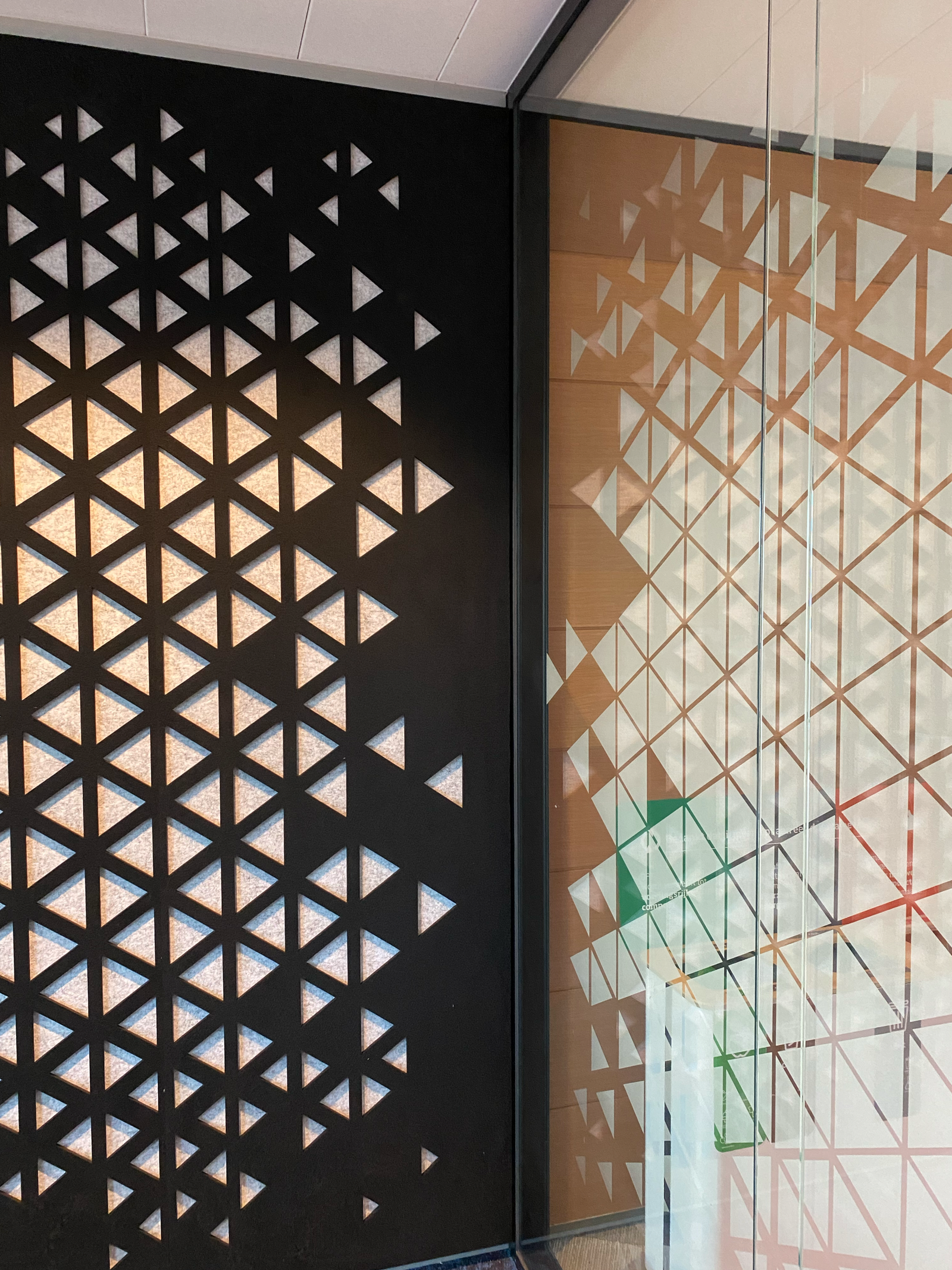 Geometric pattern with triangular cutouts on a black wall, mirrored on a glass surface, creating a modern, abstract design.