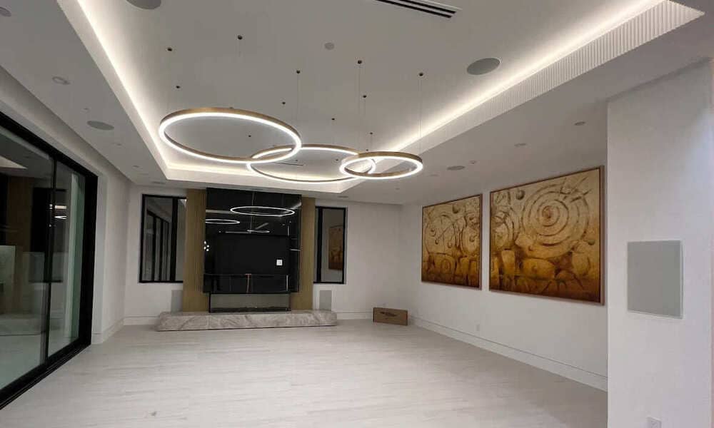 A modern, spacious interior with circular ceiling lights, abstract wall art, large windows, and light wood flooring.