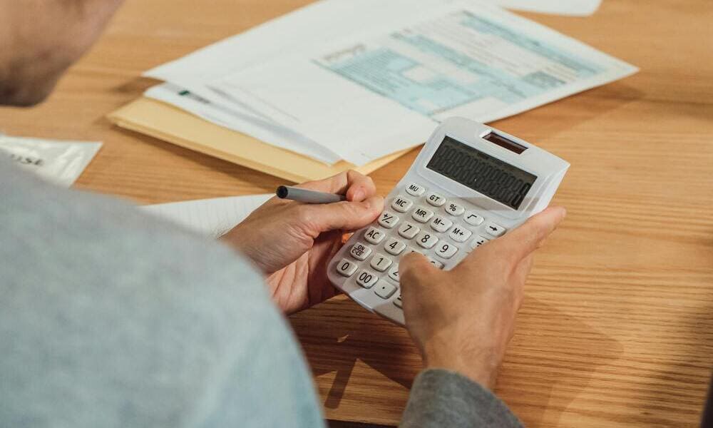 Person using a calculator at a wooden desk with papers and envelopes nearby.