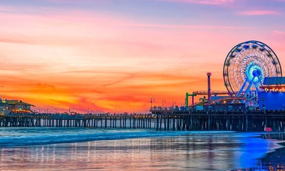 A vibrant sunset over a beach pier with a lit Ferris wheel, reflecting on the water.