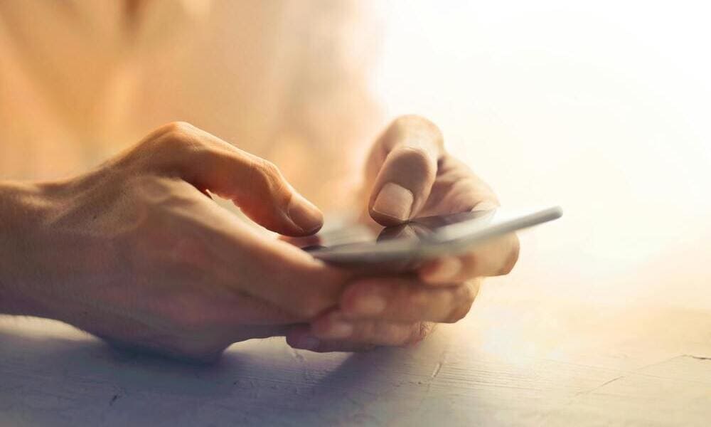 Hands holding and using a smartphone, with a soft focus background and warm lighting.