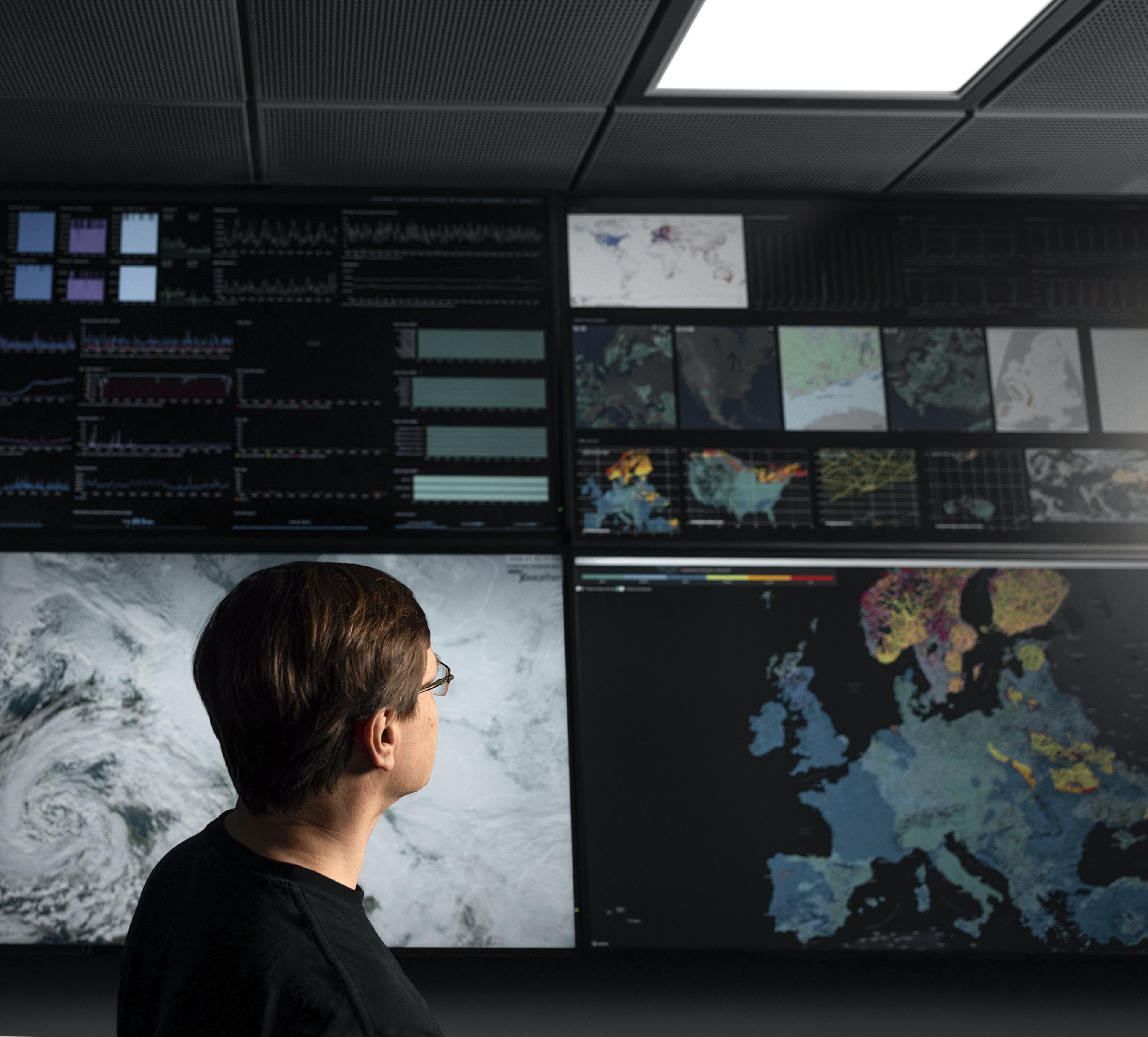 A person views large screens displaying weather maps and data analyses in a monitoring room.