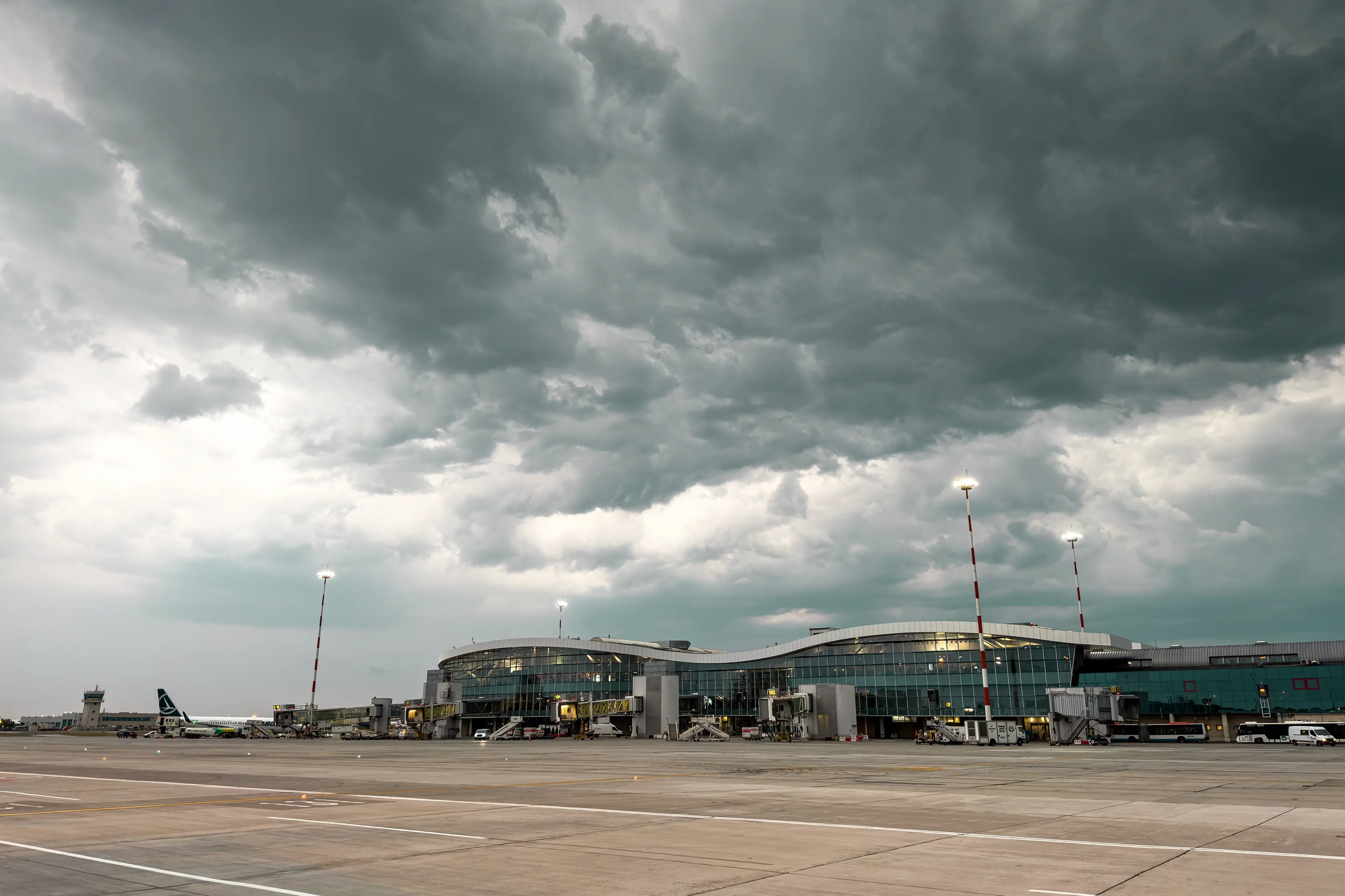 An airport terminal under a dramatic, cloudy sky with parked planes and runway lights glowing.