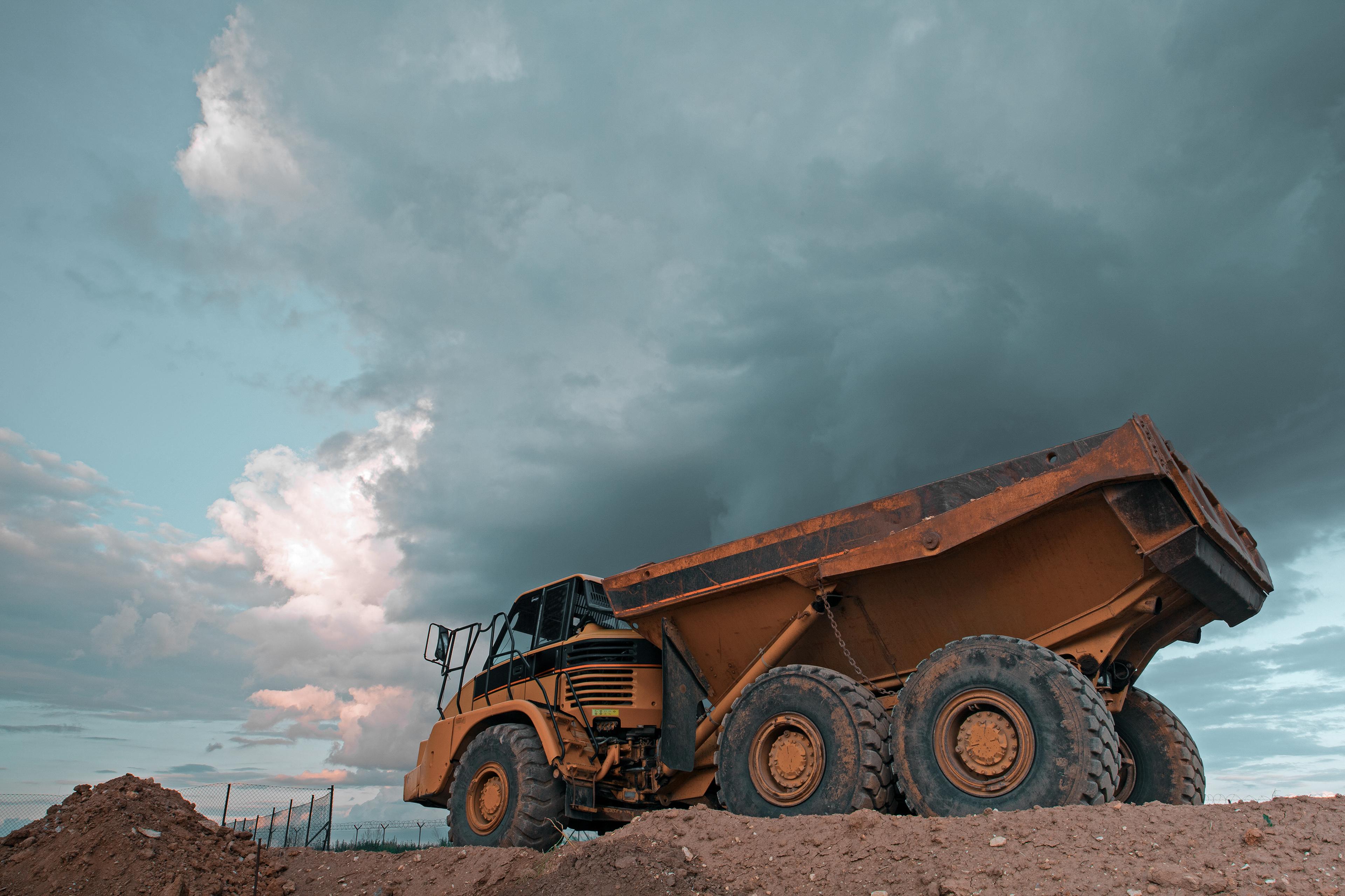 A large yellow dump truck parked on dirt with dark storm clouds looming in the background.