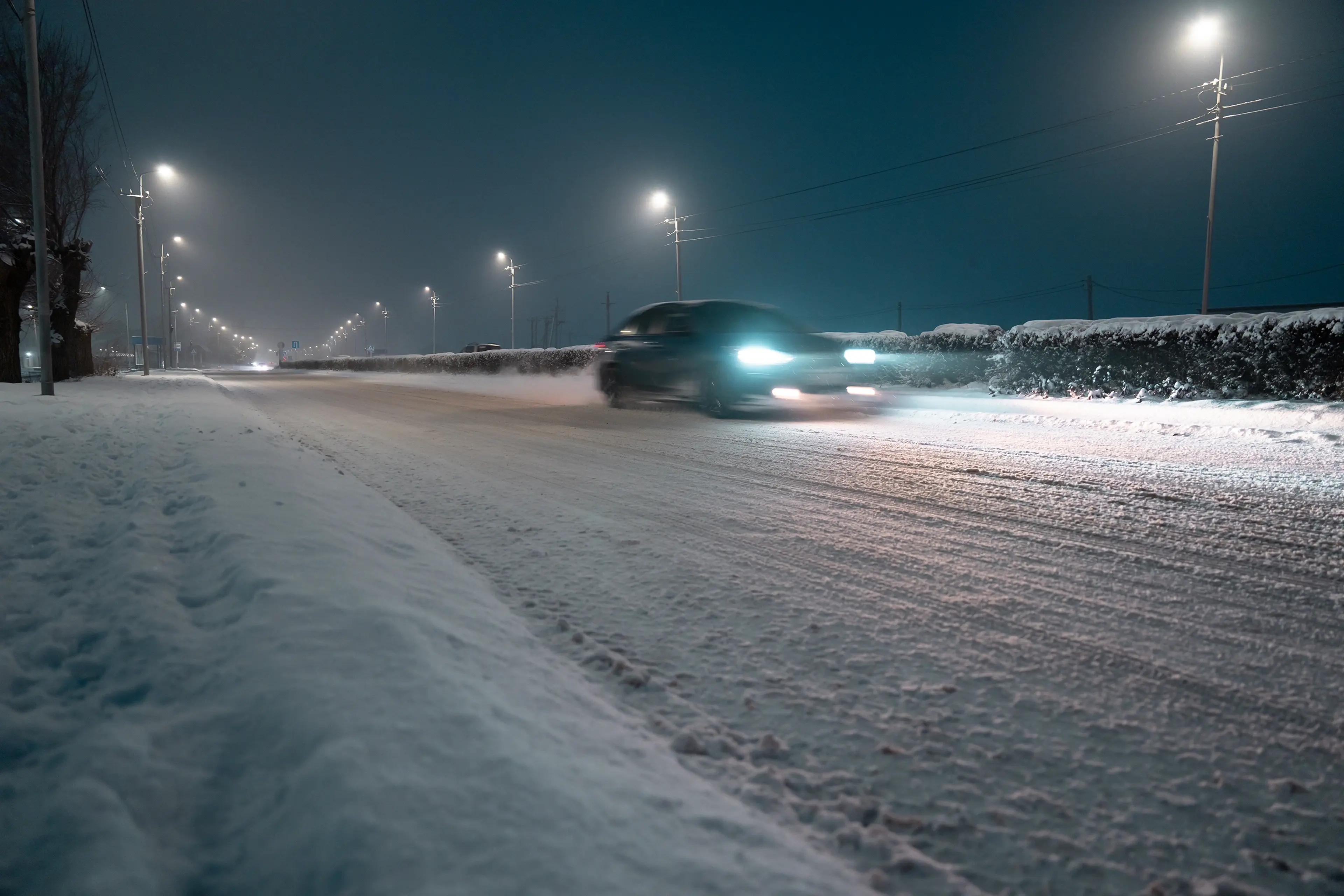 Car speeding down a snow-covered road at night, illuminated by streetlights, creating a blurred motion effect.