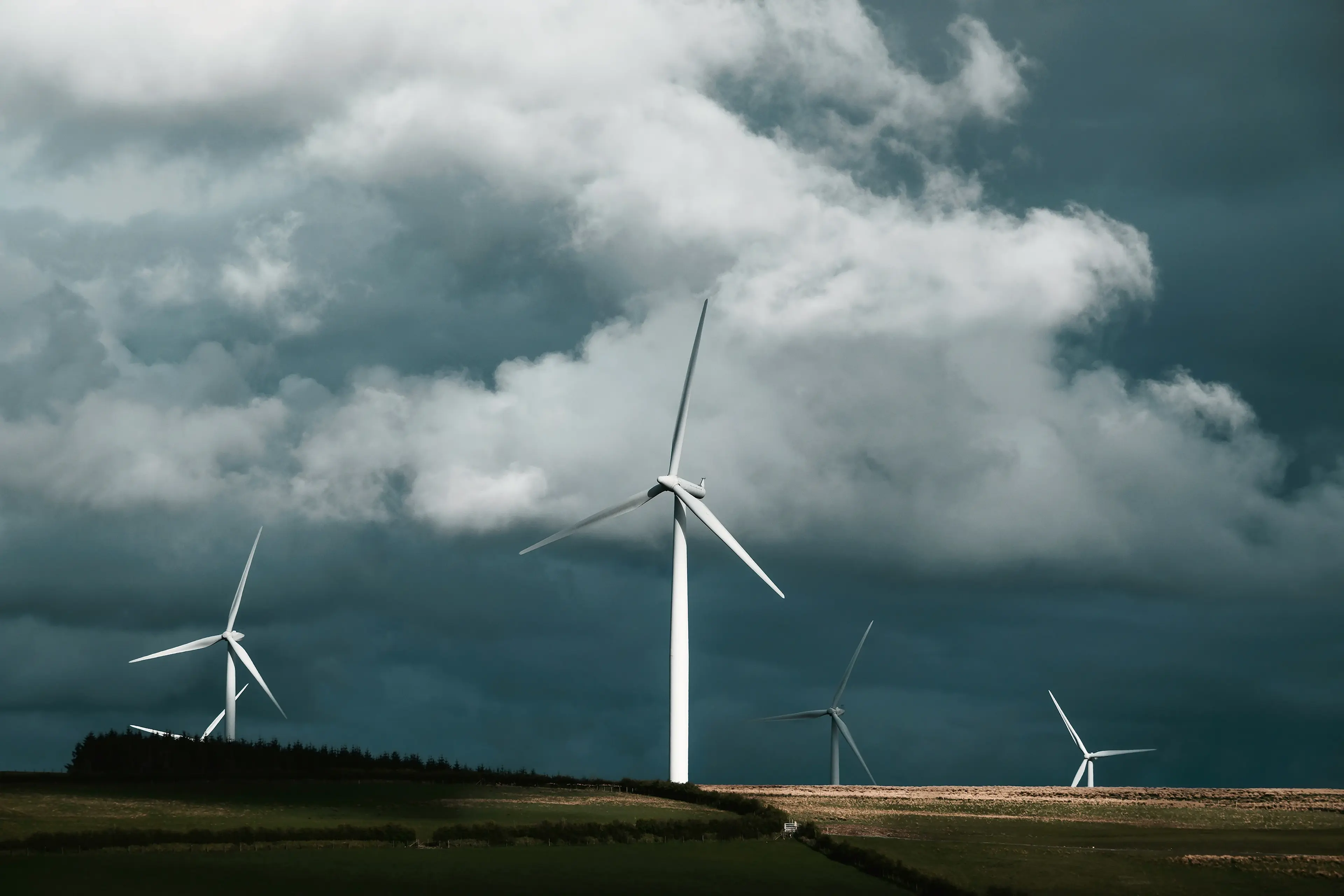 Wind turbines stand in a field under dramatic cloudy skies.