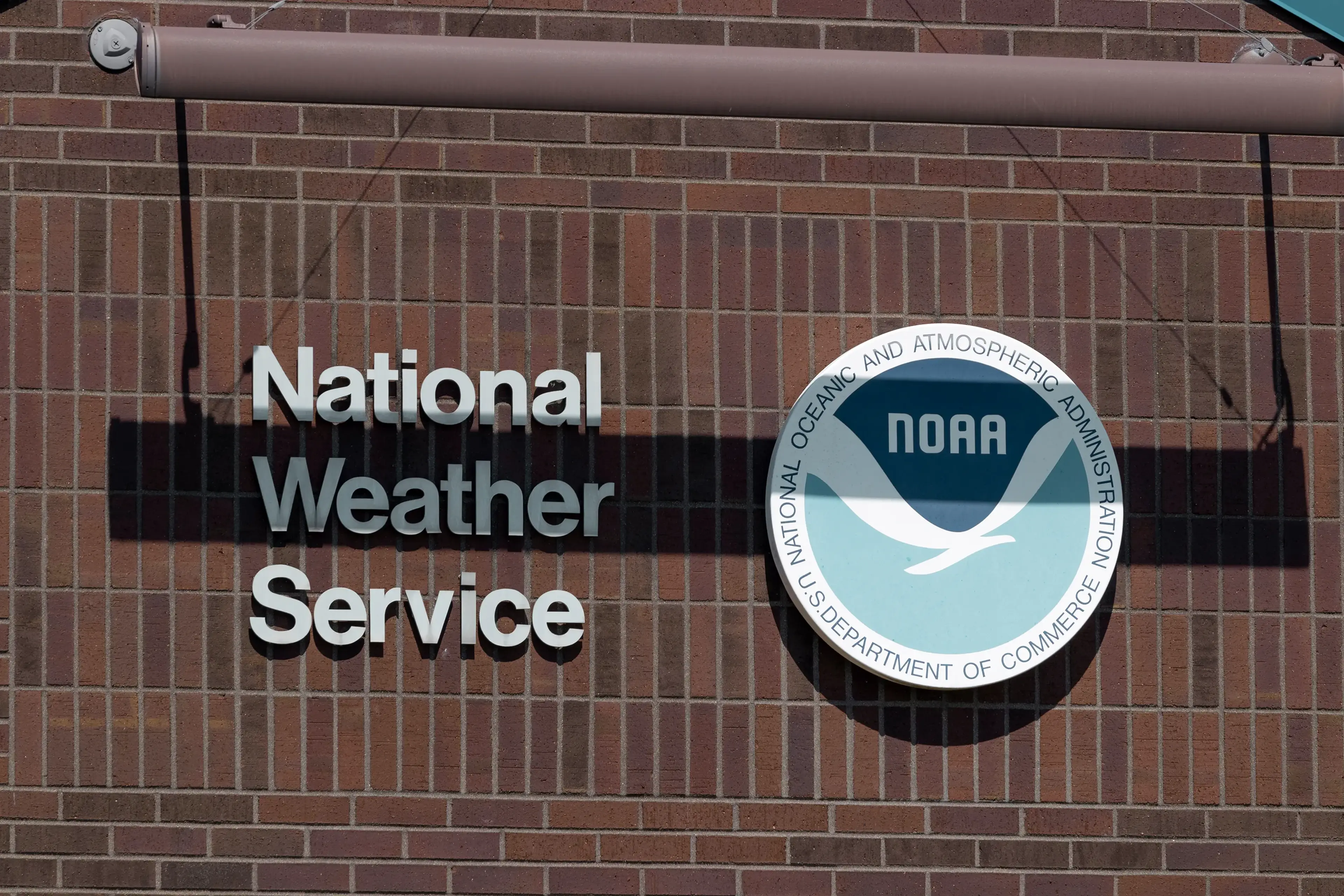 National Weather Service sign with NOAA logo on a brick wall, featuring white lettering and a circular emblem.