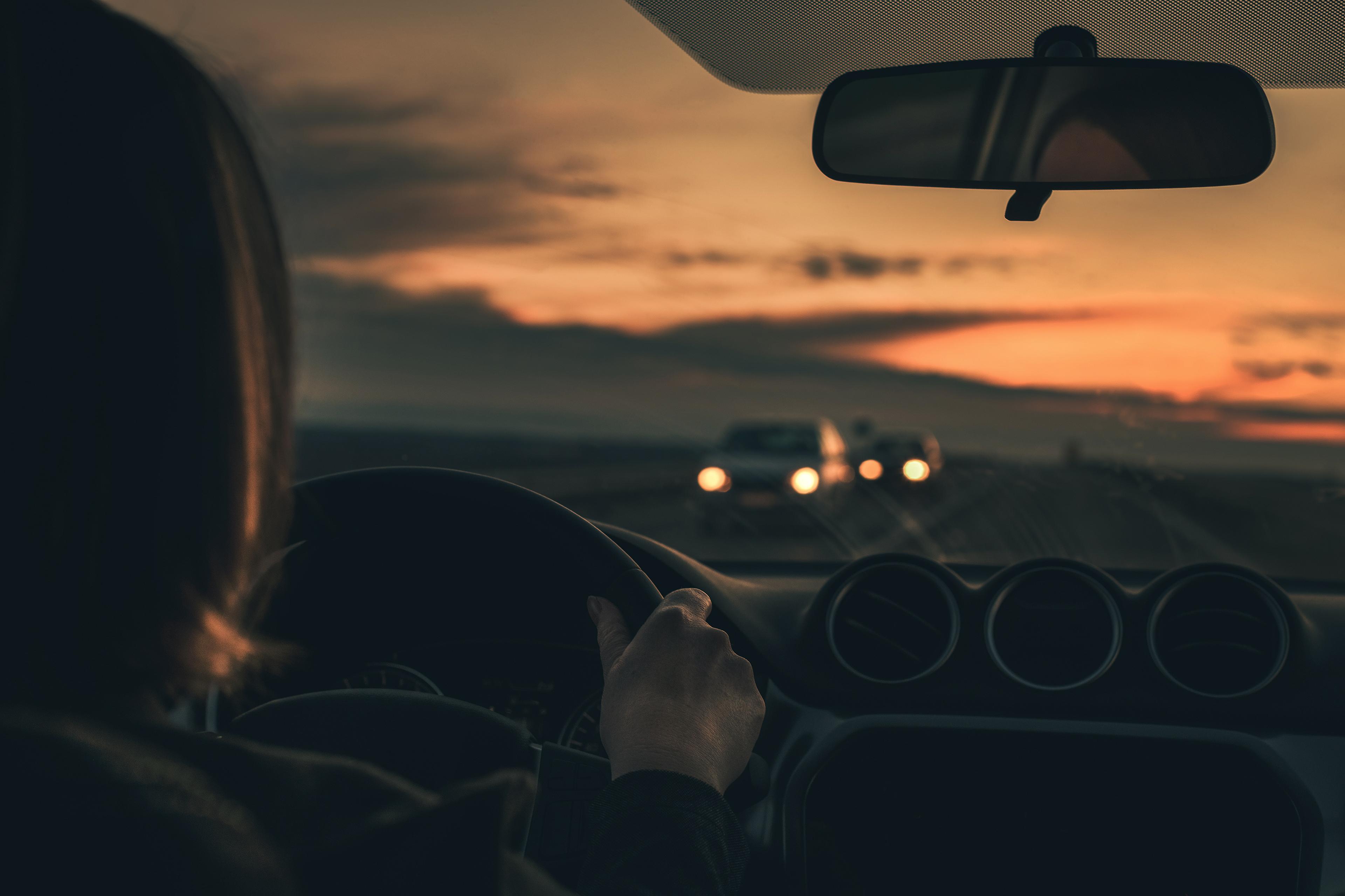 View from inside a car at dusk, focusing on a driver's hands on the wheel and oncoming cars with headlights.