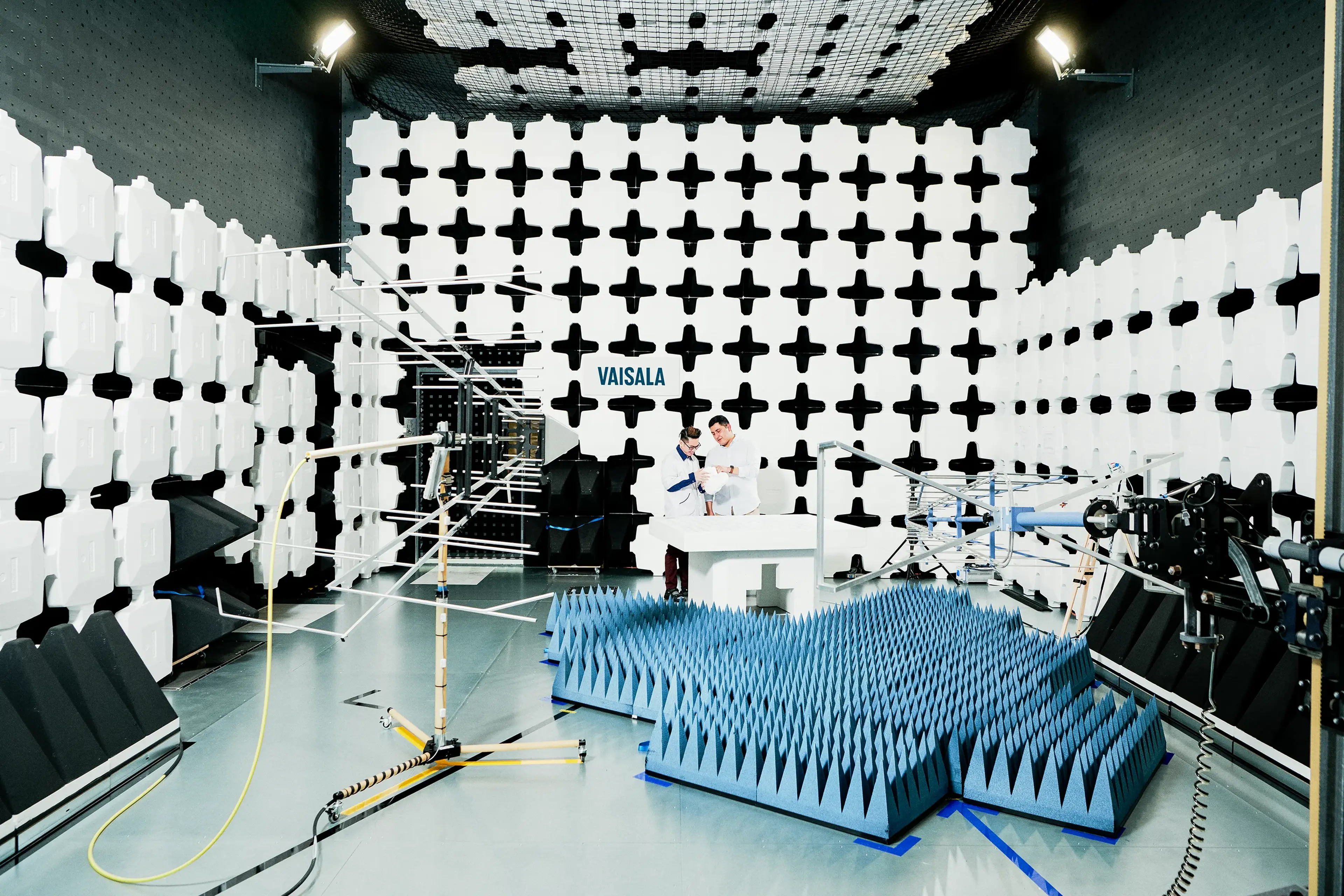 Two scientists in a white, grid-patterned testing lab with equipment and sensors at Vaisala.