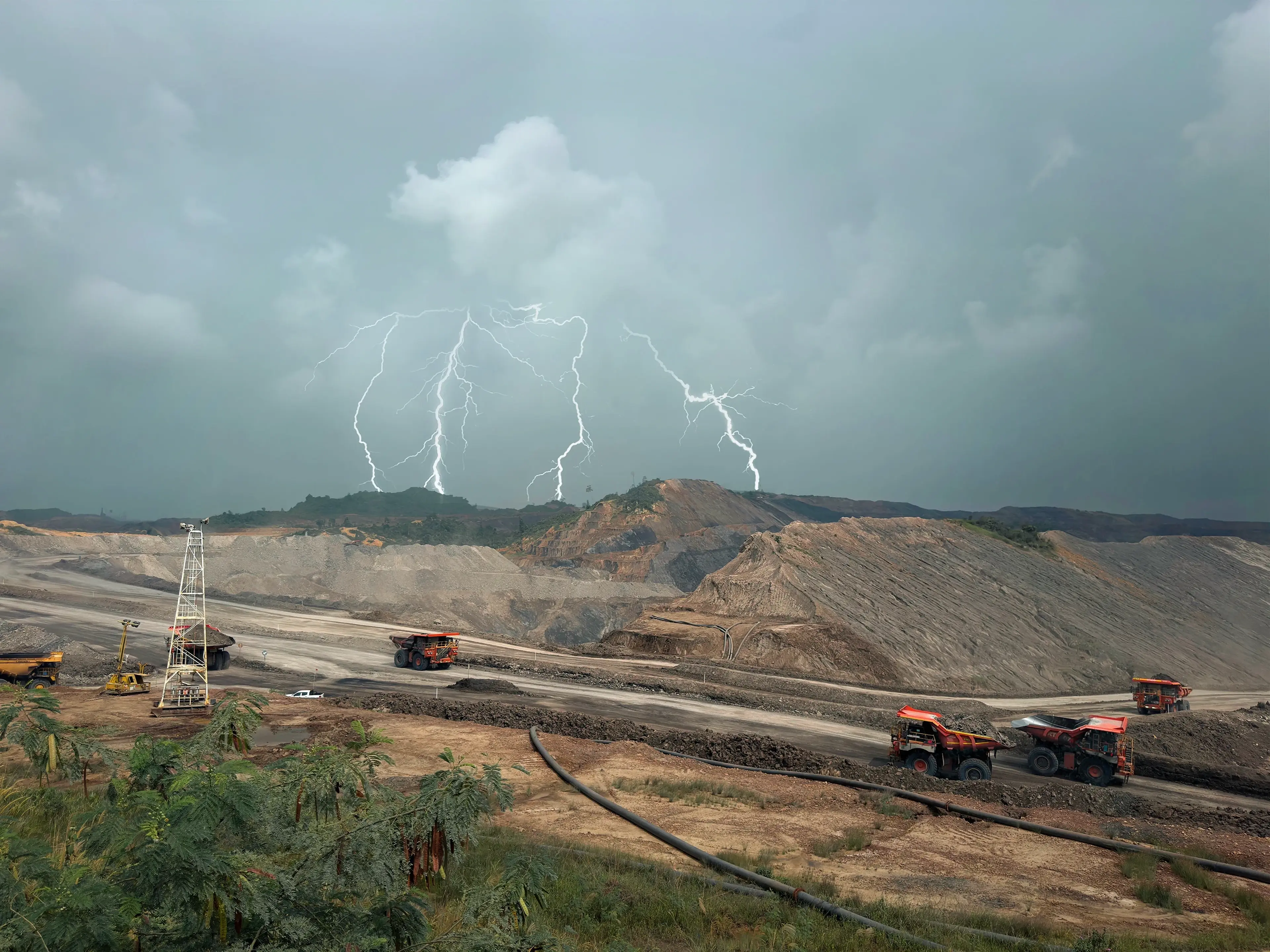 Lightning storm over a mining site with large trucks on dirt paths, and a cloudy sky in the background.