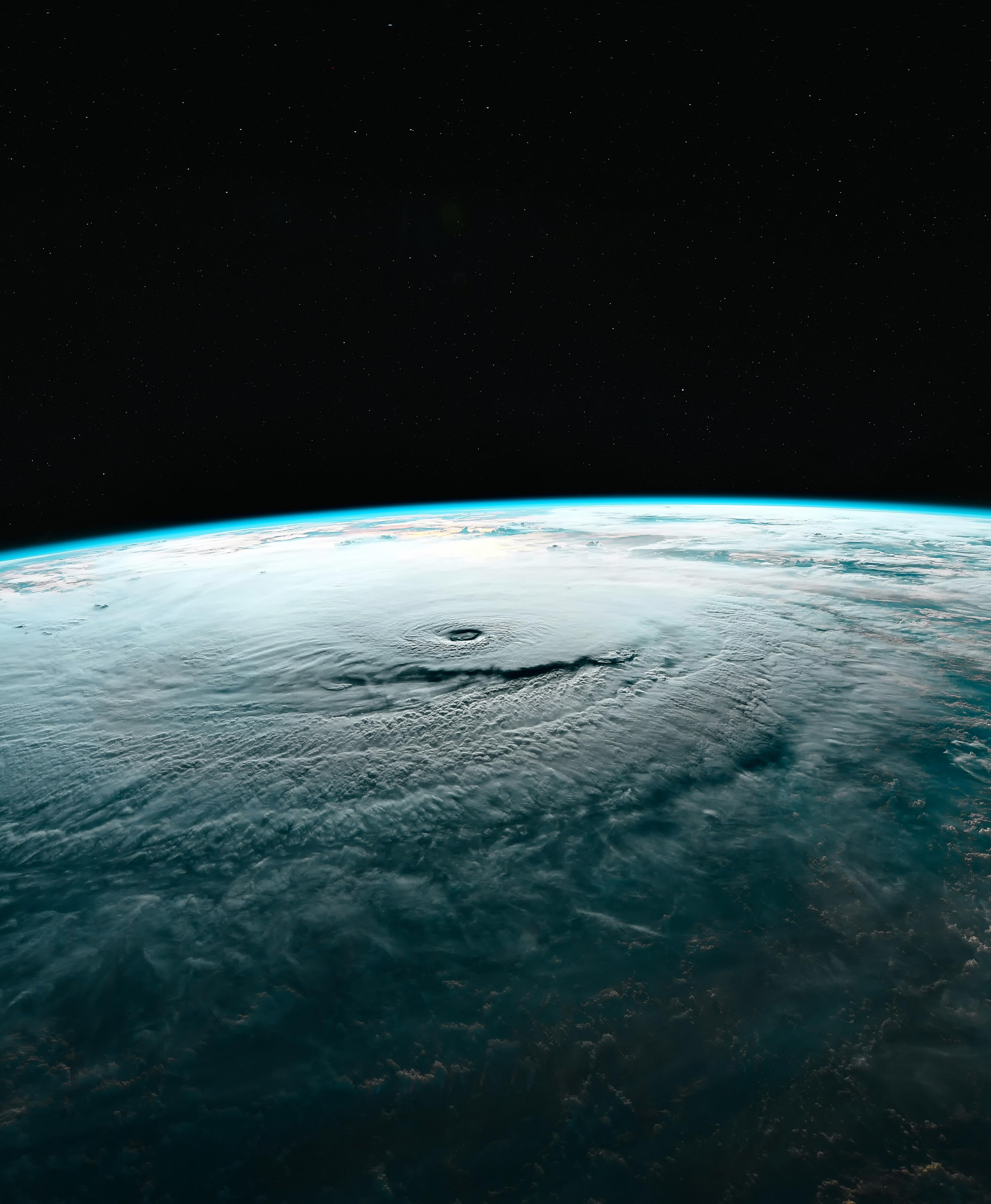 Aerial view of a massive storm system on Earth, showcasing a large swirling cloud formation under a starry sky.