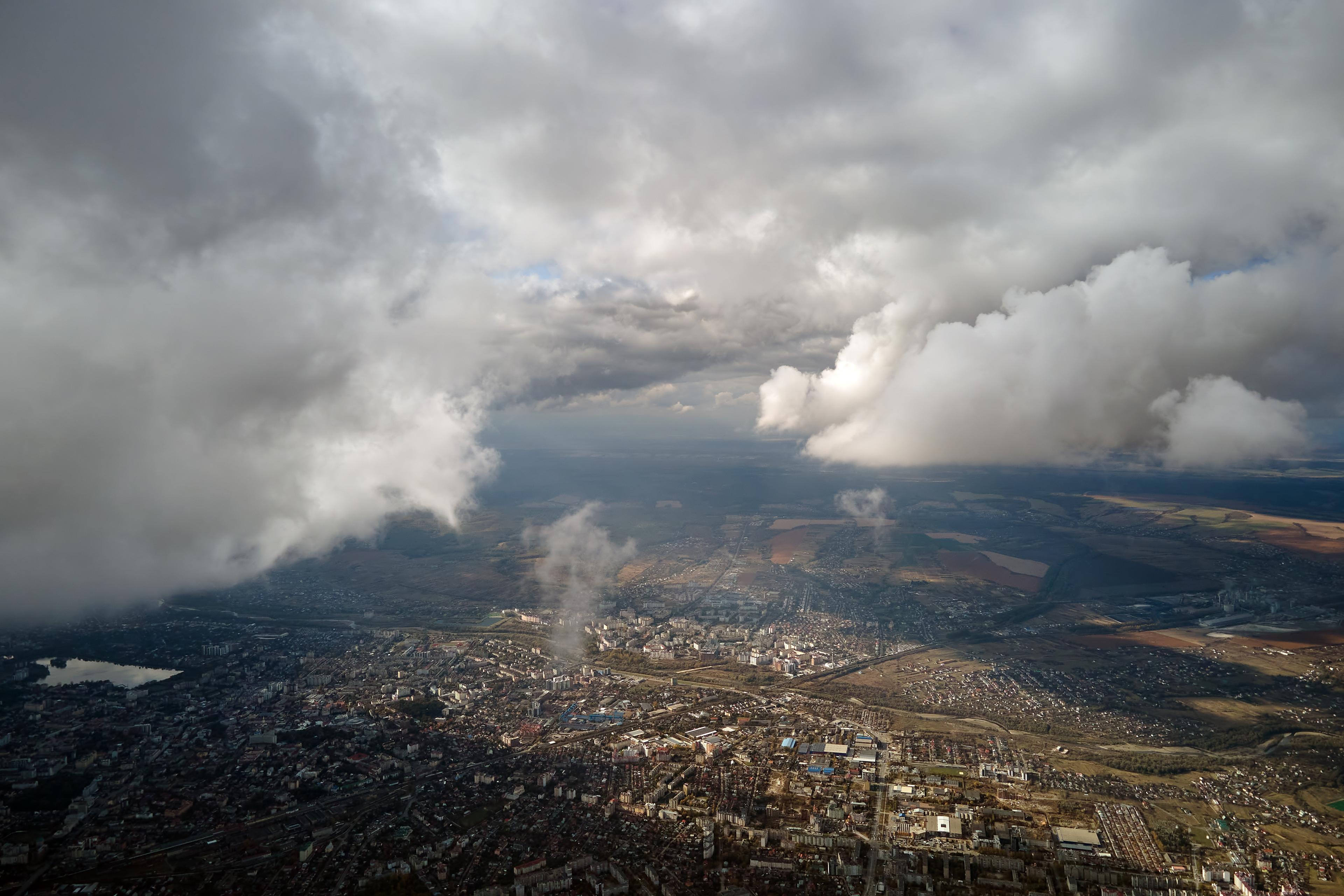 Aerial view of a city surrounded by landscape, covered by thick clouds, with patches of sunlight highlighting fields and urban areas.