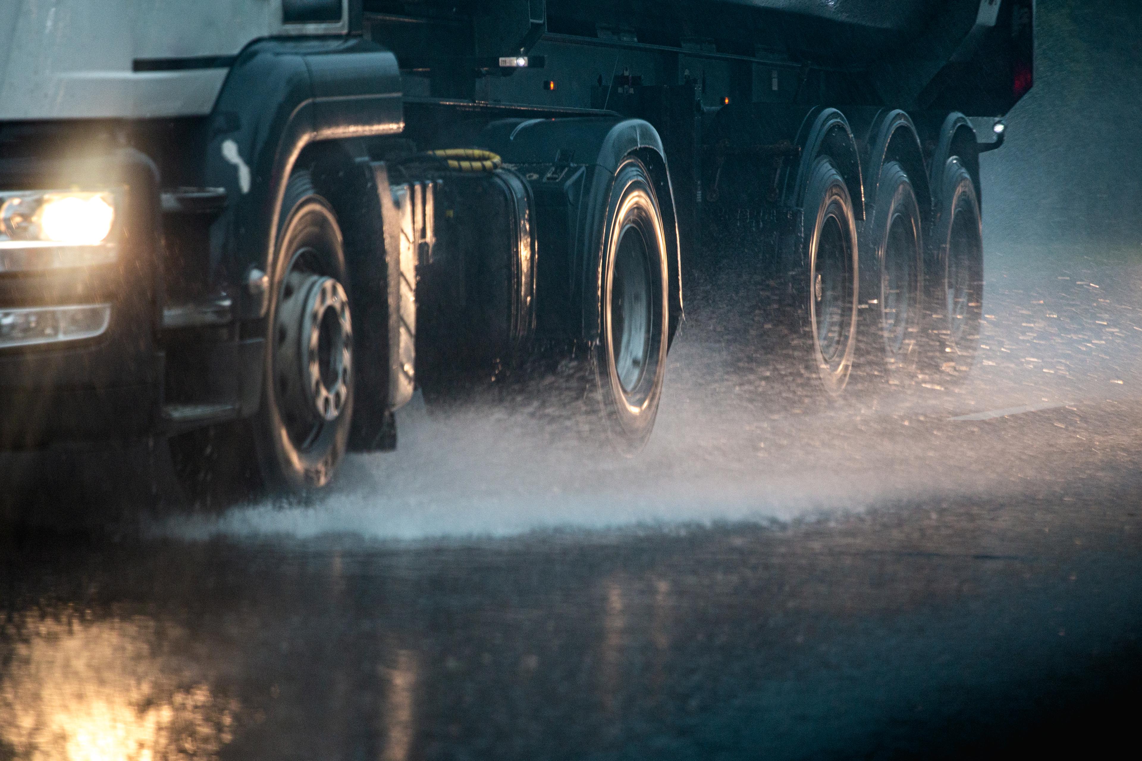 A large truck drives through heavy rain on a wet road, with water splashing from its tires.