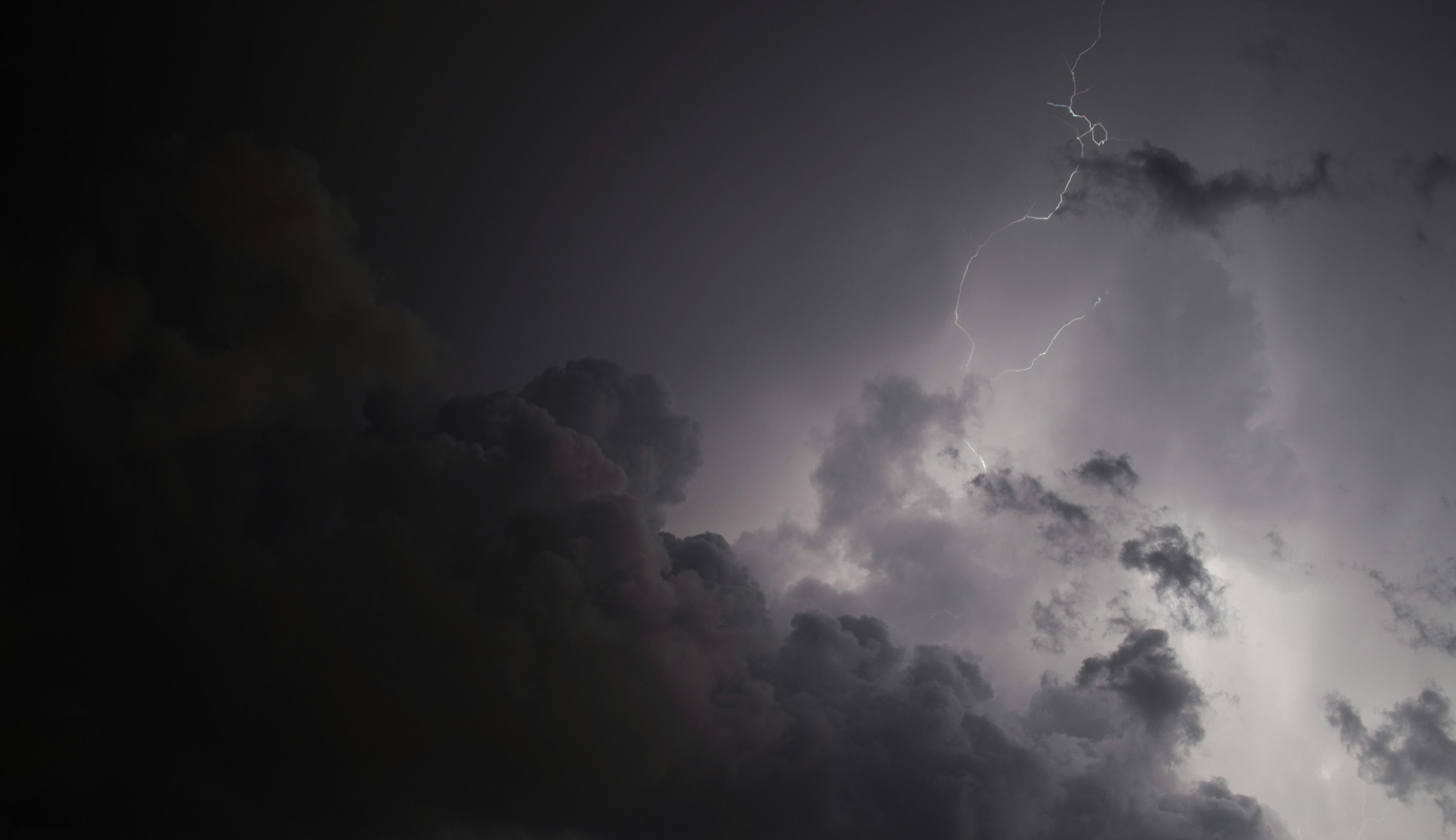 Dark storm clouds with a bright lightning bolt illuminating the sky, creating a dramatic contrast between light and shadow.