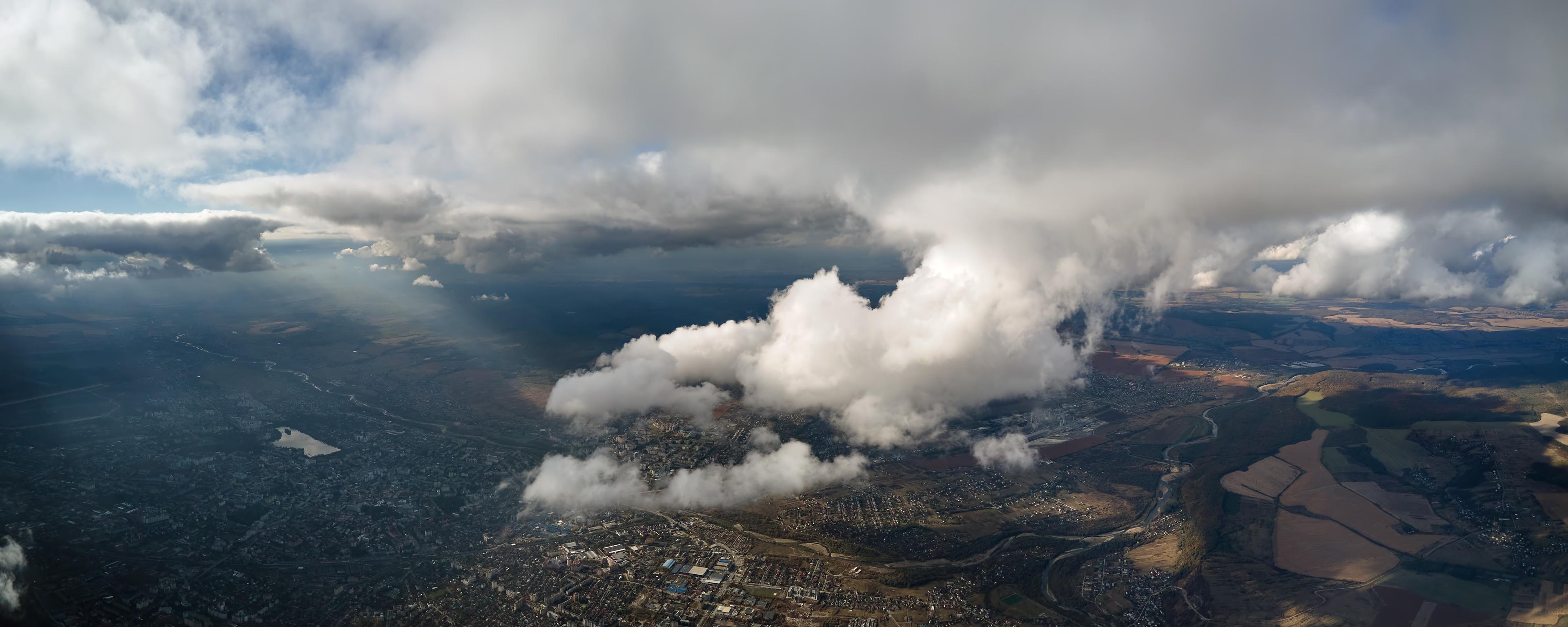 Aerial view of a cityscape beneath scattered clouds, with sunlight breaking through, casting dramatic shadows on the landscape below.
