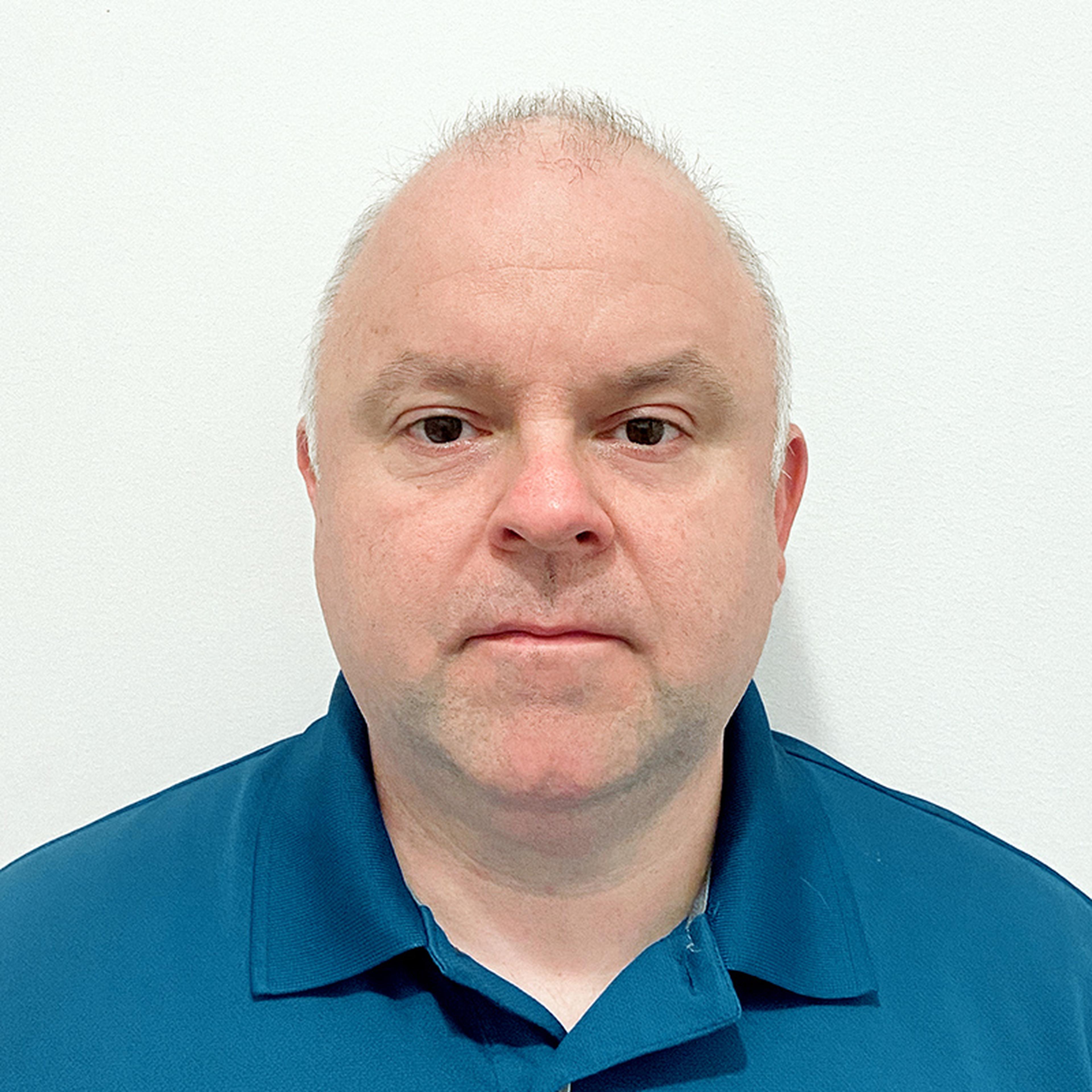 A man with short hair wearing a blue collared shirt against a plain white background.