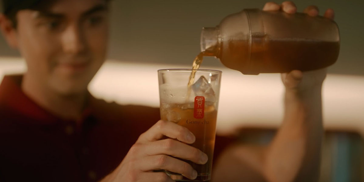 Hand pouring freshly brewed Gong Cha iced tea over ice in a tall glass, ready to customise.
