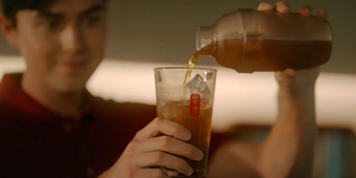 Hand pouring freshly brewed Gong Cha iced tea over ice in a tall glass, ready to customise.